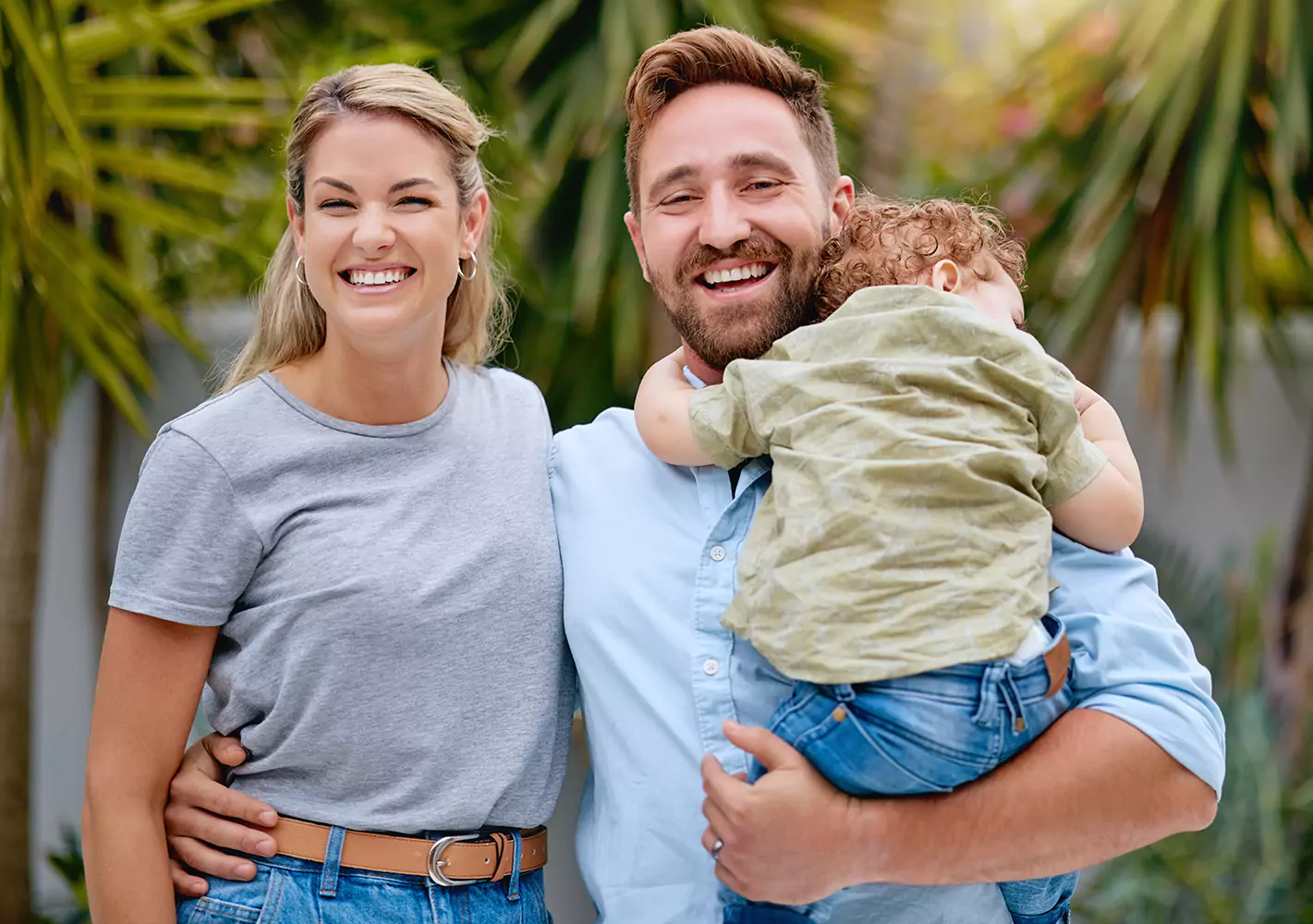 Happy couple with arms around each other, husband holding young child