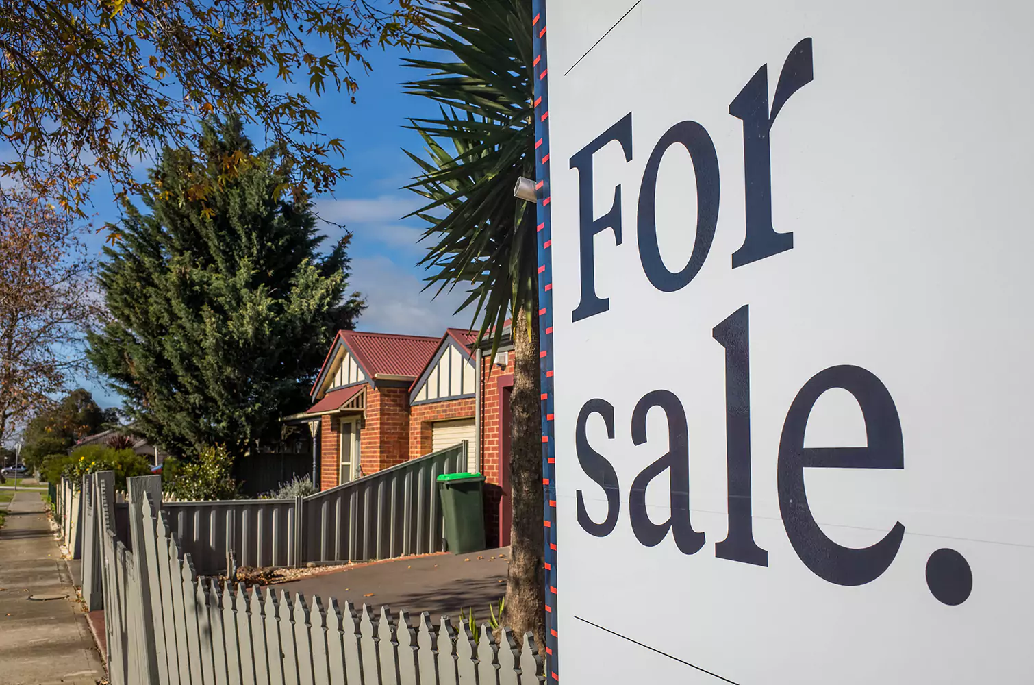 Close up of a white 'for sale' sign out the front of a house on a suburban street